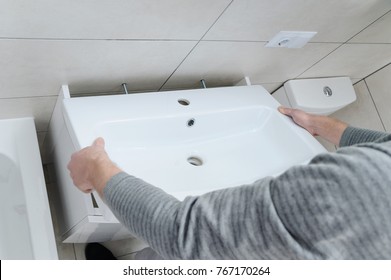 A man is setting the washbasin over the cabinet in the bathroom.