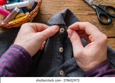 man sews a button to his shirt - Powered by Shutterstock