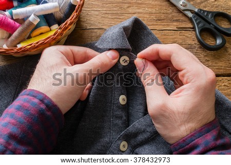 man sews a button to his shirt