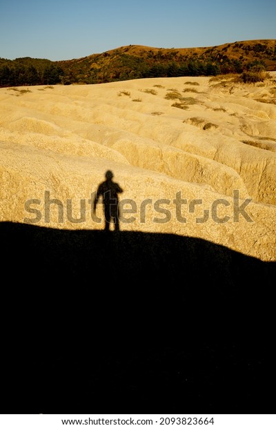 Man shadow\
silhouette projected over a dried mud ravine yellowed by the\
setting sun at Berca Mud Volcanoes\
reservation