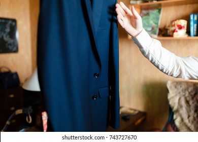 The Man Shakes Off The Dust And Straightens His Clothes With A Dark Blue Suit Hanging On A Hanger In The Office. Dress Is Formal In The Office. A Set Of Classic Menswear.