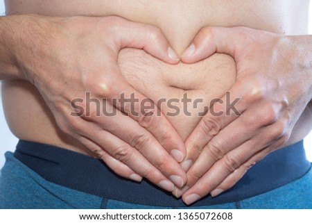 Man shapes hands to the heart symbol over a fat belly