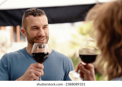A man in sharp focus enjoys a glass of red wine, sharing a special moment with his partner, subtly visible in the foreground.