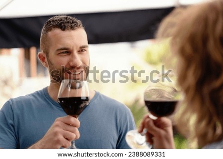 A man in sharp focus enjoys a glass of red wine, sharing a special moment with his partner, subtly visible in the foreground.