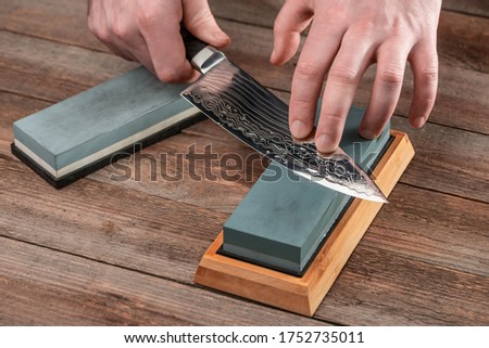 Man sharpening a Japanese chef's knife with a wet whetstone on a rustic wooden table.