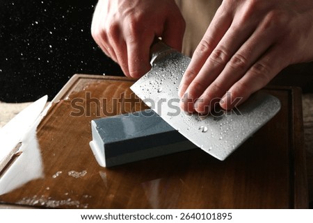 Man sharpening knife with sharpener on wooden table, closeup