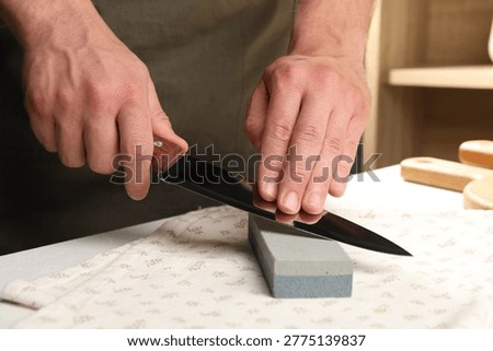 Man sharpening knife at white table in kitchen, closeup