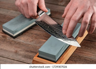 Man sharpens a Gyuto knife using a whetstone on a rustic wooden table. Japanese knife with Damascus steel.