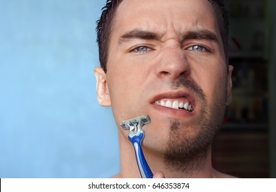 A Man Shaves His Face Without Cream Or Foam, Experiencing Pain And Suffering. Half Face Shaved Half Overgrown With A Thick Beard.