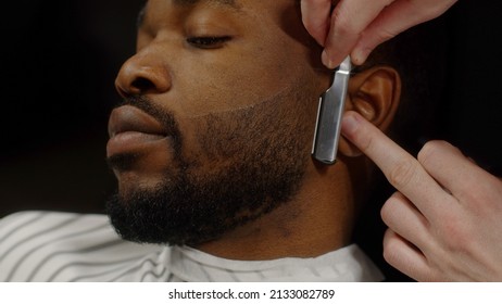 Man shaving beard of african american man with straight razor in barbershop - Powered by Shutterstock