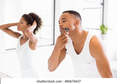 Man shaving with razor in bathroom and woman in background - Powered by Shutterstock