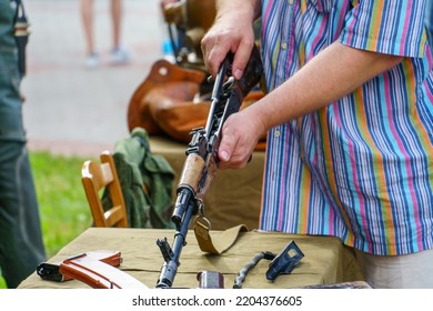 A Man In A Shirt Is Holding A Loaded Kalashnikov Assault Rifle. Exhibition Of Weapons For The Russian Army. A Military Man With A Gun In His Hands.