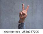 Man in a shirt showing gesture V means victory, peace sign or protest sign, close-up against a concrete wall