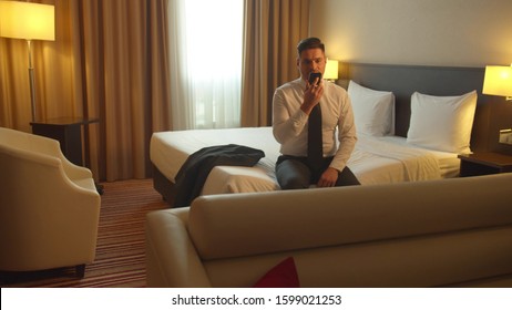 Man In Shirt And Tie Sit On The Bed In Hotel And Record Voice Message On Phone