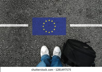 a man with a shoes and backpack is standing on asphalt next to flag of European Union and border - Shutterstock ID 1281497575