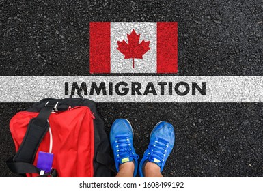 Man in shoes with bag standing next to line with word IMMIGRATION and flag of Canada on asphalt road - Shutterstock ID 1608499192