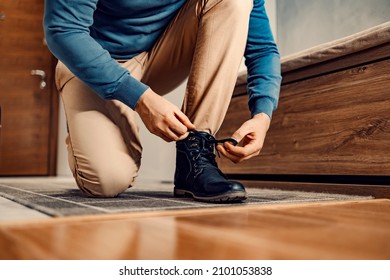 A Man In Shoes Or Boots. A Man Is Kneeling At Home, Tying His Shoelace, And Preparing To Go Outside.