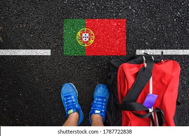 a man with a shoes and travel bag is standing on asphalt next to flag of Portugal and border 