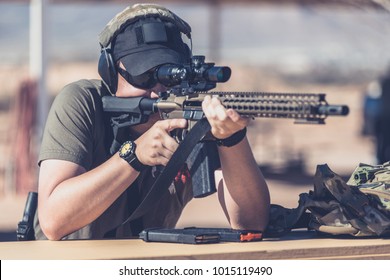 Man shooting assault style rifle at shooting range in desert resting on bench front