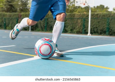 Man Shooting The Ball On The Blue Soccer Field. Close Up Image Of A Young Boy Wearing Blue Shorts And White Socks Kicking A Red, White And Blue Ball.