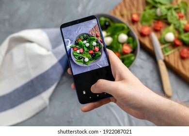 Man shooting fresh vegetable salad with mozzarella and spinach on cell phone camera. Cooking, blogging and healthy eating concept. - Powered by Shutterstock