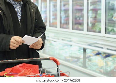 A Man With Shopping Cart And List, Grocery Store Refrigerator In Background