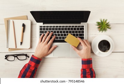 Man shopping online with credit card and laptop with blank screen. Top view of human hands, laptop keyboard, coffee and notebook on white wooden table background - Powered by Shutterstock