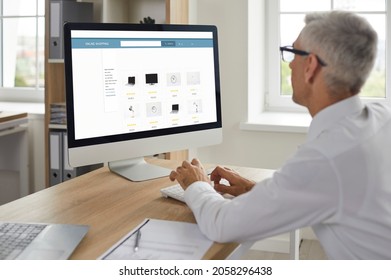 Man shopping online. Senior businessman sitting at work desk, looking at computer display, browsing Internet gadget outlet, buying new office equipment, adding items to cart, paying with credit card