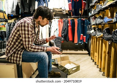 Man Shopping In An Outdoor Store. Male Buying Mountain Boots. Shopper In Sports Store Select Hiking Shoes. Customer Purchase Of Footwear For Adventures. Man Trying Mountaineering Boots At Travel Shop.