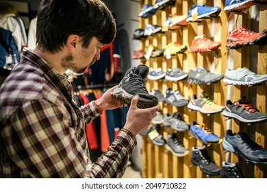 Man Shopping In An Outdoor Store. Male Buying Mountain Boots. Shopper In Sports Store Select Hiking Shoes. Customer Purchase Of Footwear For Adventures. Man Trying Mountaineering Boots At Travel Shop.