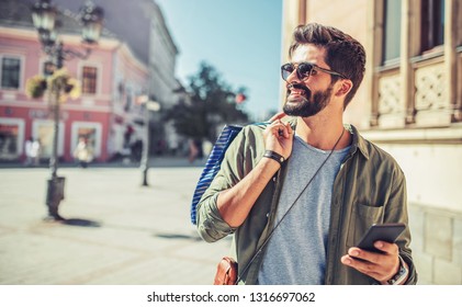 Man in shopping. Smiling man with shopping bags walking down the street. Consumerism, lifestyle concept - Powered by Shutterstock