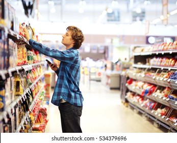  Man shopping in supermarket reading product information.Using smarthone - Shutterstock ID 534379696