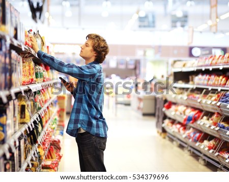  Man shopping in supermarket reading product information.Using smarthone