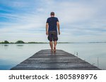 Man in short cargo pants walking on wooden pier and observes the surface of lake, Varazdin lake, Croatia
