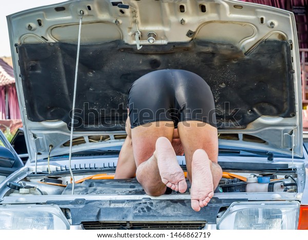 A man in shorts repairs cars in\
the field. Autotravel concept. Car breakdown. Car\
repair.