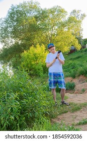 Man In Shorts Stands On The Beach Holding A Go Pro Camera. Myakinino, Moscow Oblast, Russia 06/2019