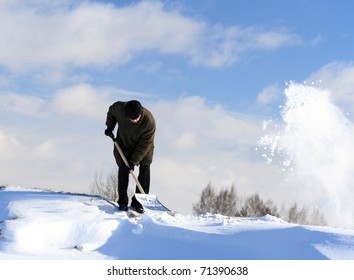 A Man With A Shovel Removing Snow From A Roof