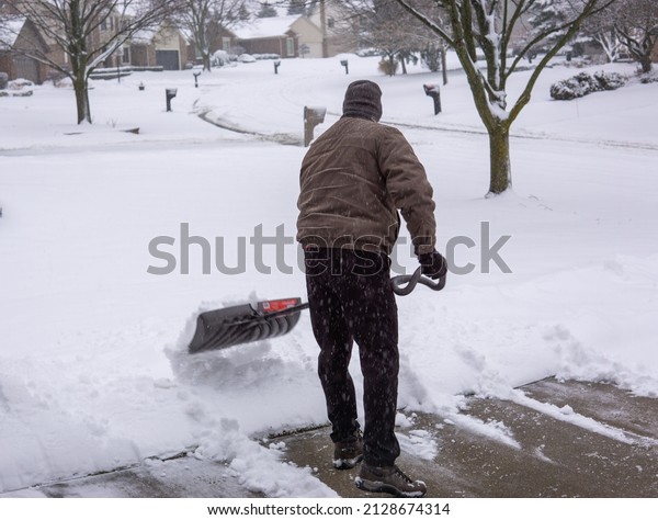 Man\
shoveling snow from driveway in winter back\
turned