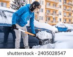 A man shovels snow in front of a snowy car.