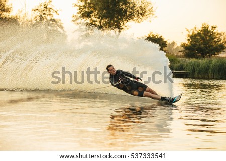 Man show of his water skiing skill on a lake. Athlete doing stunts on wakeboard.