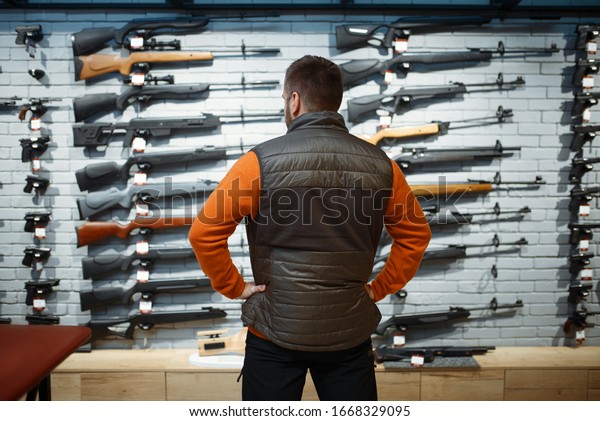 Man at\
showcase with rifles, back view, gun\
shop