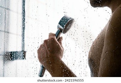 Man in shower. Water splash drops on bath cabin stall glass. Faucet head in hand. Public gym, hotel or home bathroom. Washing skin and body. Hot or cold spa douche. Happy person in washroom. - Powered by Shutterstock