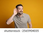 Man showing hand to ear gesture on orange background