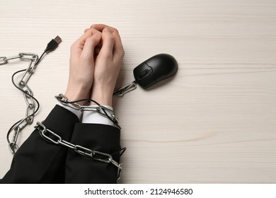 Man showing hands chained with computer mouse cable at white wooden table, top view. Internet addiction