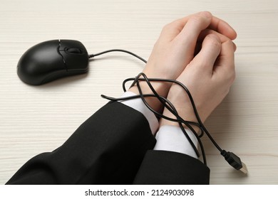 Man showing hands tied with computer mouse cable at white wooden table, closeup. Internet addiction