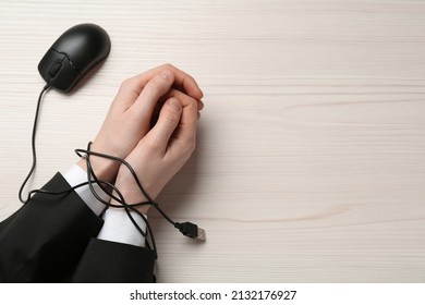 Man showing hands tied with computer mouse cable at white wooden table, top view. Internet addiction
