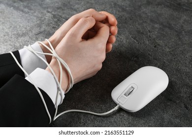 Man showing hands tied with computer mouse cable at grey table, closeup. internet addiction