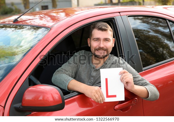 Man showing learner driver sign from new car. Get\
driving license