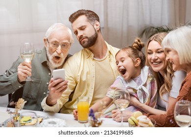 Man Showing Mobile Phone To Amazed Family During Easter Dinner