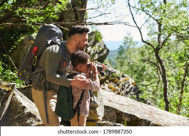 Man showing something to little boy while he looking through the binoculars during their trip in the forest - Powered by Shutterstock